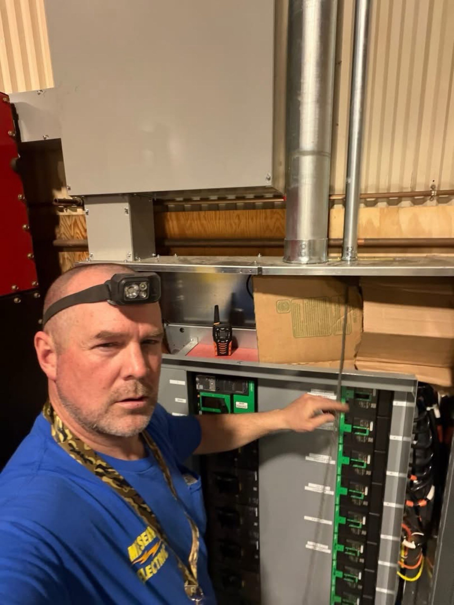 Jay Meserve, in a Meserve Electric shirt, working at an open electrical panel